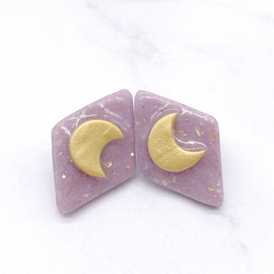 two pastel purple, diamond-shaped stud earrings. Each earring features a delicate crescent moon design in the center.